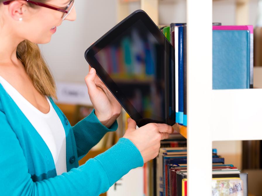 Billedet viser en kvinde, som trækker en tablet ud af en bogreol