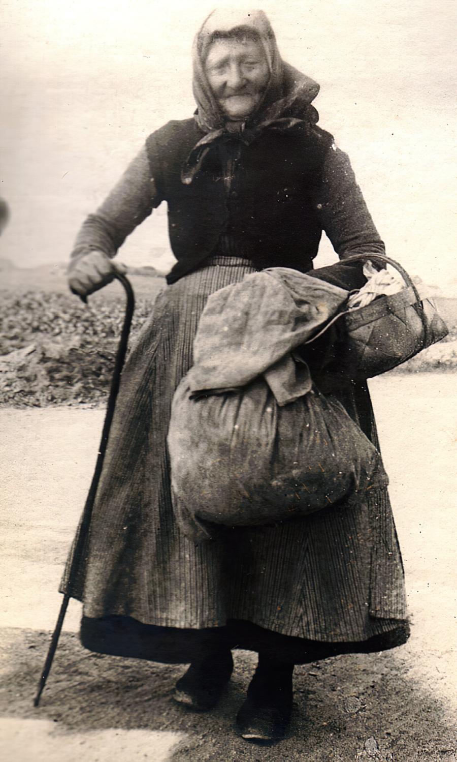 En ældre kvinde, der ser mega slidt og træt ud, står med sin stok