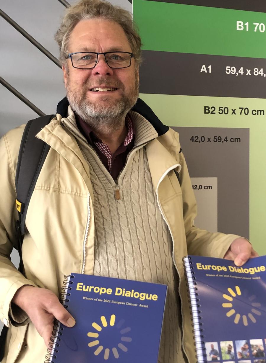 Uffe Hvidkjær viser stolt nogle bøger eller lignende frem, der reklamerer for EU - en dejlig dag på jobbet, tydeligvis