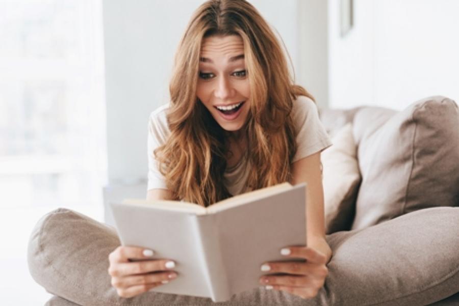 Billede af kvinde der ser overrasket ud, mens hun læser i en bog.