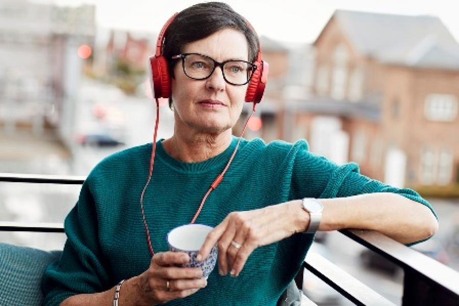 Billede af en kvinde der sidder på sin terrasse med en kop kaffe og lytter til en podcast.
