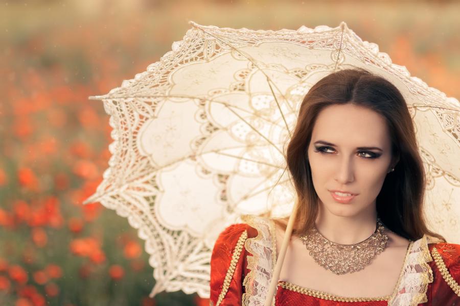 Billedet forestiller en kvinde i en rød, gammeldags kjole. Hun har en hvid parasol til beskyttelse mod solen.