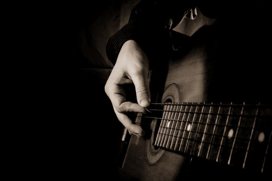Billedet forestiller en guitar og en hånd der med en plekter spiller. Billedet er holdt i sorthvidt.