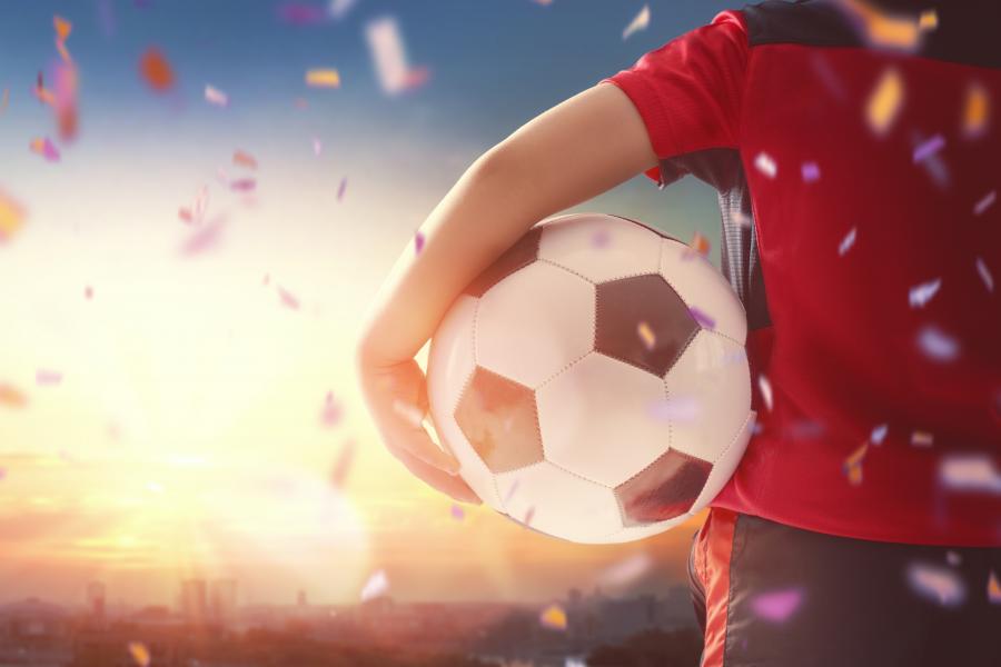 Billedet forestiller en dreng med en fodbold under armen. Han står med ryggen til, og foran ham er der en smuk solnedgang.