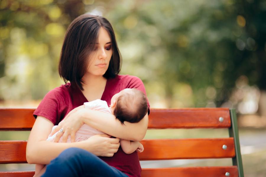 Billedet forestiller en mørkhåret kvinde, der sidder med et spædbarn i armene. Kvinden kigger på barnet og ser lidt utilpas ud.